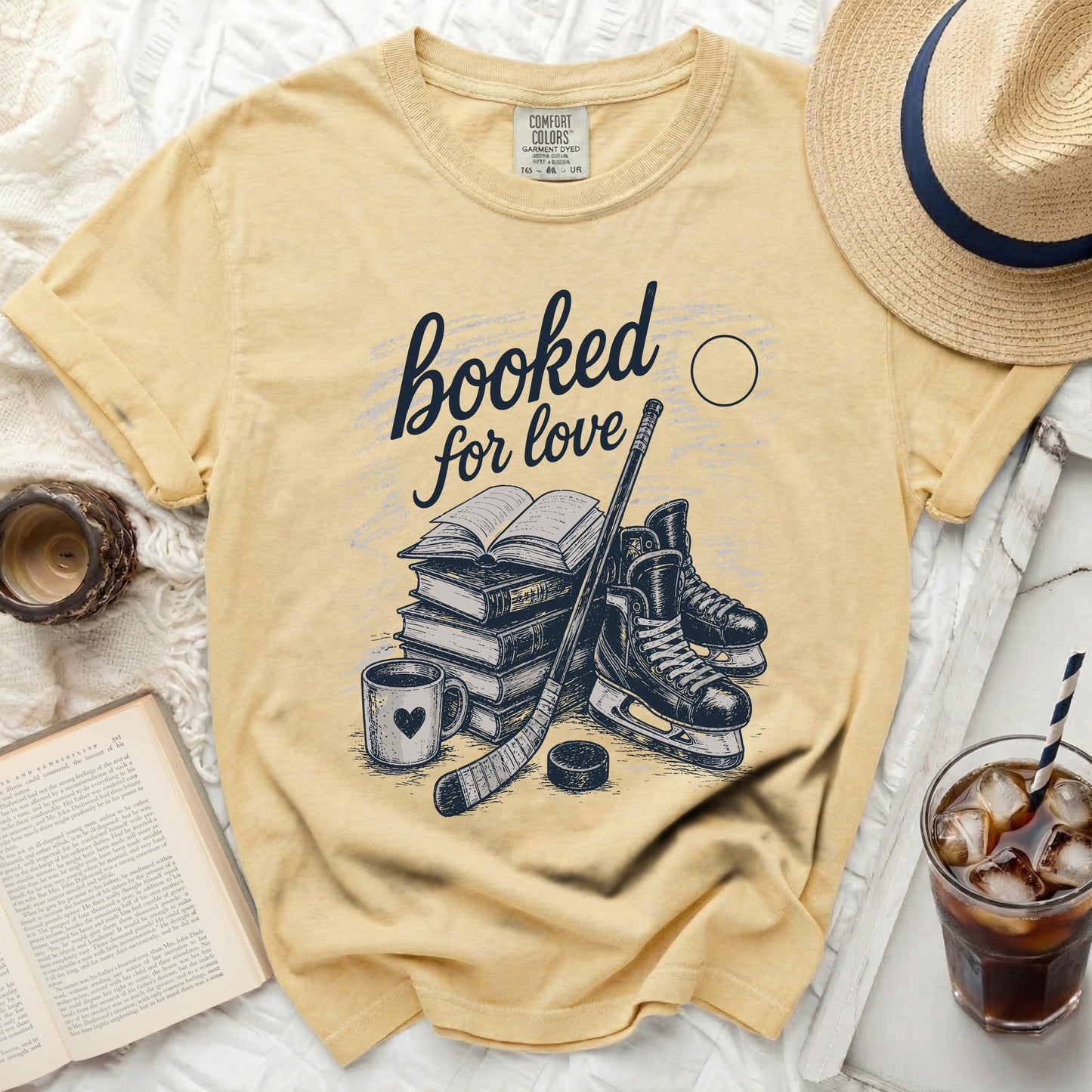 Yellow t-shirt with stacked books, hockey skates, puck, stick, and coffee.