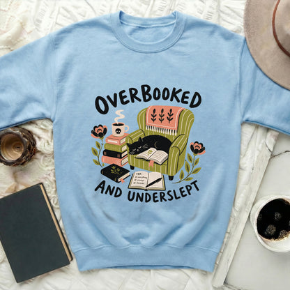 Light blue sweatshirt with "Overbooked and Underslept" text featuring a cat on an armchair.