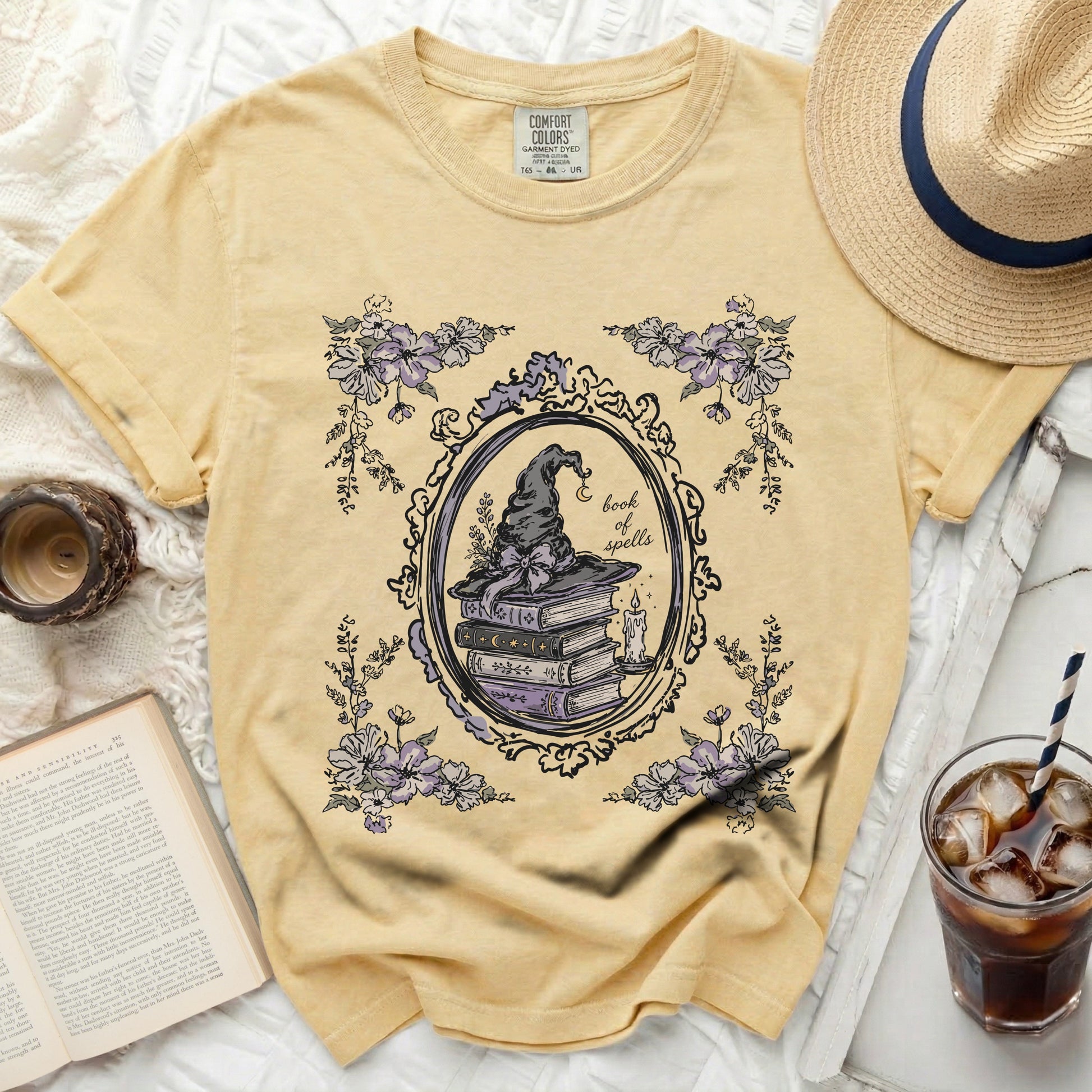 Yellow t-shirt with floral frame, witch hat, books, and "book of spells" text.