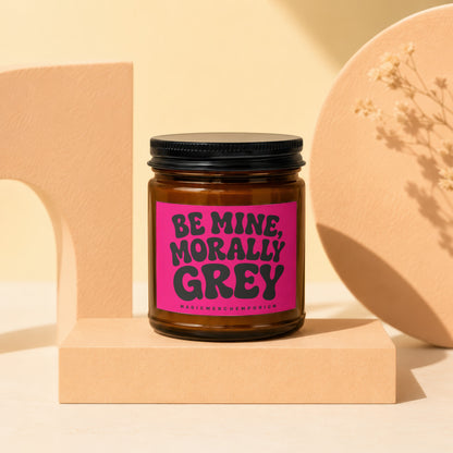 Amber jar candle with pink label saying "Be Mine, Morally Grey".