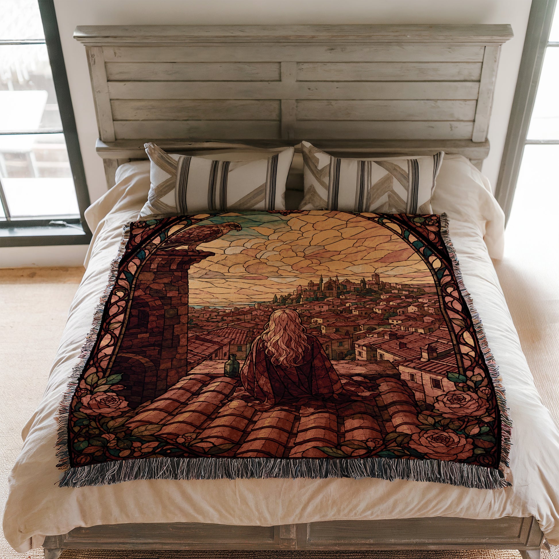 a large bed with a decorative blanket that depicts a cityscape. The blanket has a colorful, stained glass-like design with a woman sitting on a rooftop, overlooking the city.