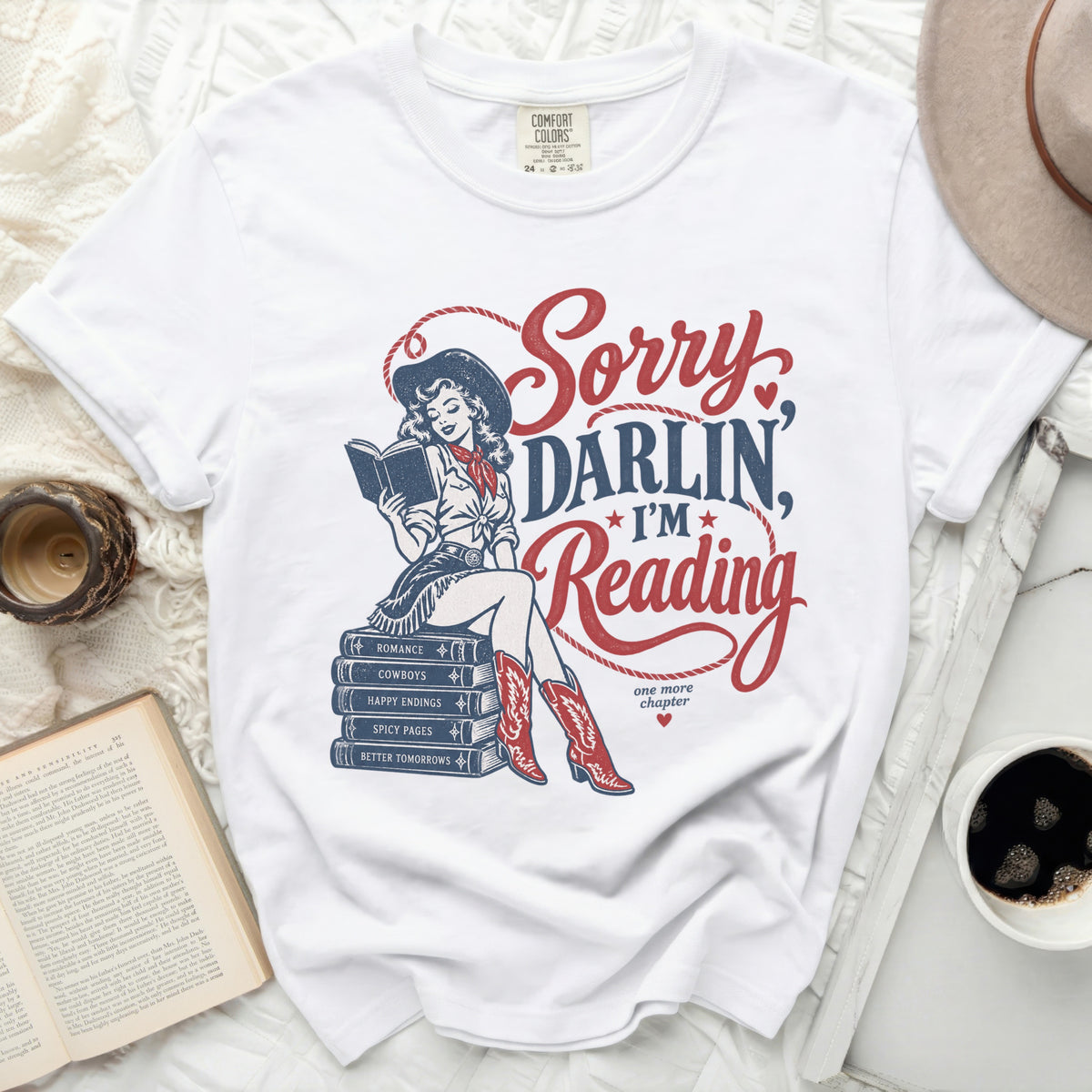 White t-shirt with "Sorry Darlin', I'm Reading" and cowboy book stack graphic.