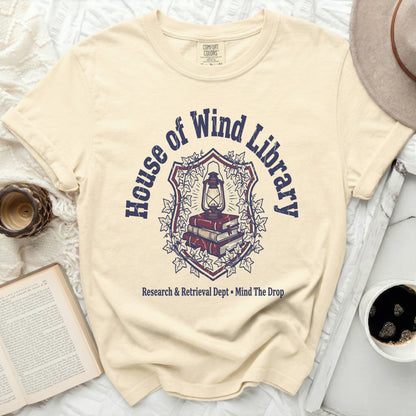 Cream t-shirt with "House of Wind Library" crest and book graphic.