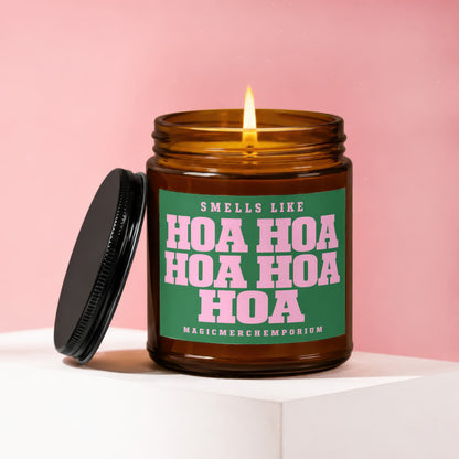 Amber jar candle with lit flame and green label that reads: "SMELLS LIKE HOA HOA HOA HOA MAGICMERCHMEPORIUM".