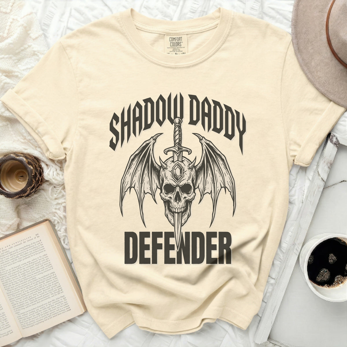 Cream t-shirt with black graphic of skull, wings, sword, and text.