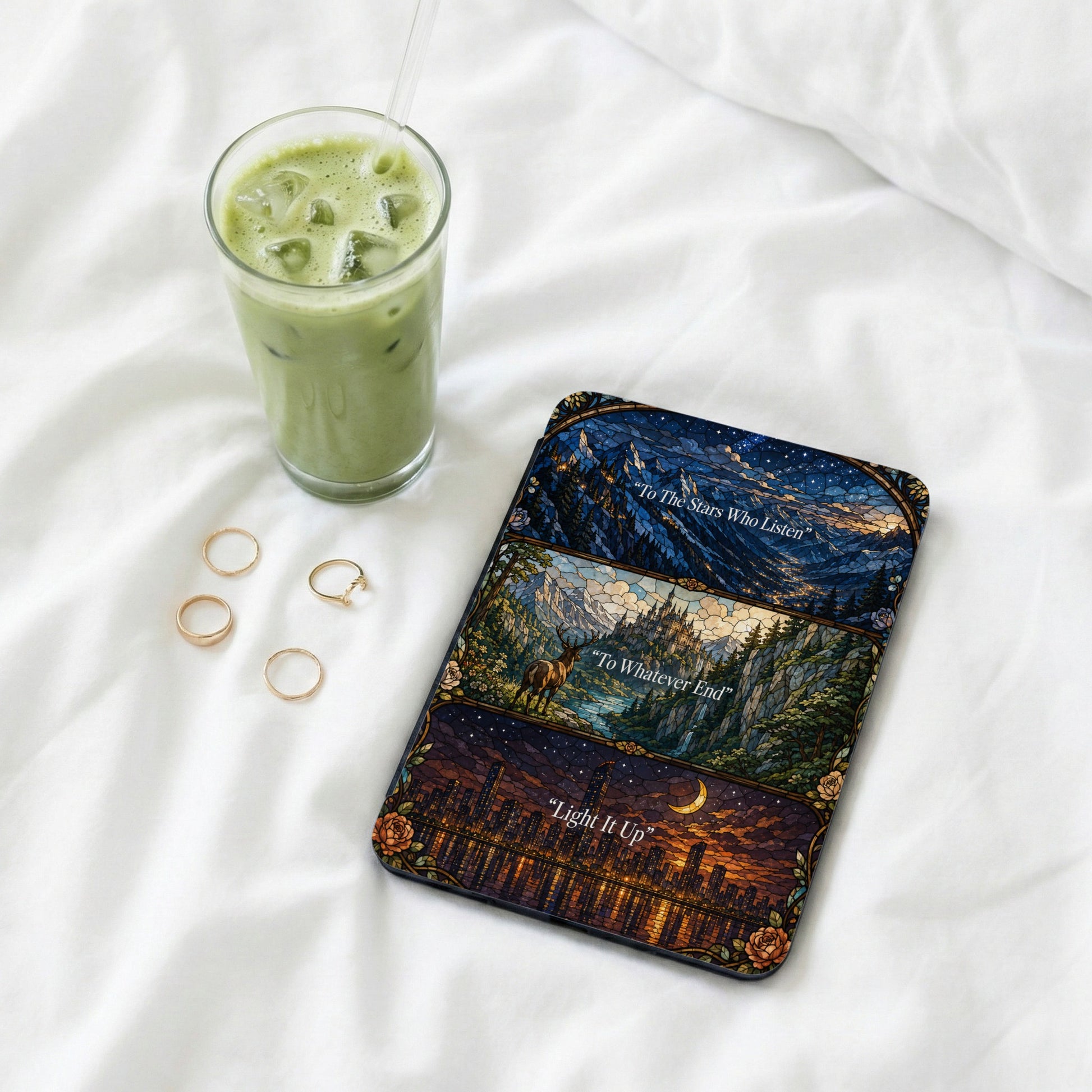 Phone case with mosaic art of night sky, castle, and city, beside iced green drink.