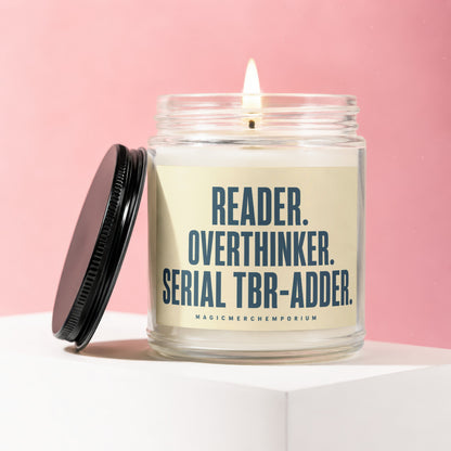 Glass candle lit with flame on a shelf, inscribed "Reader. Overthinker. Serial TBR-Adder."