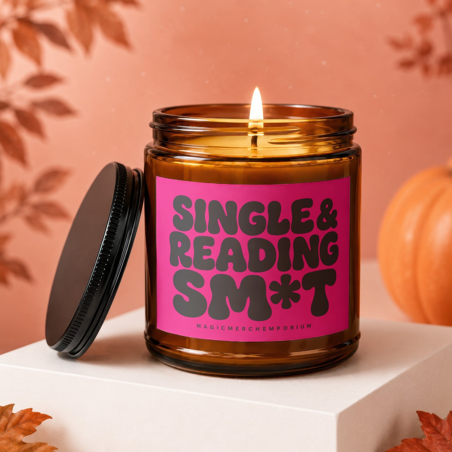 Amber candle with pink label reading "Single & Reading SM*T" on white pedestal.
