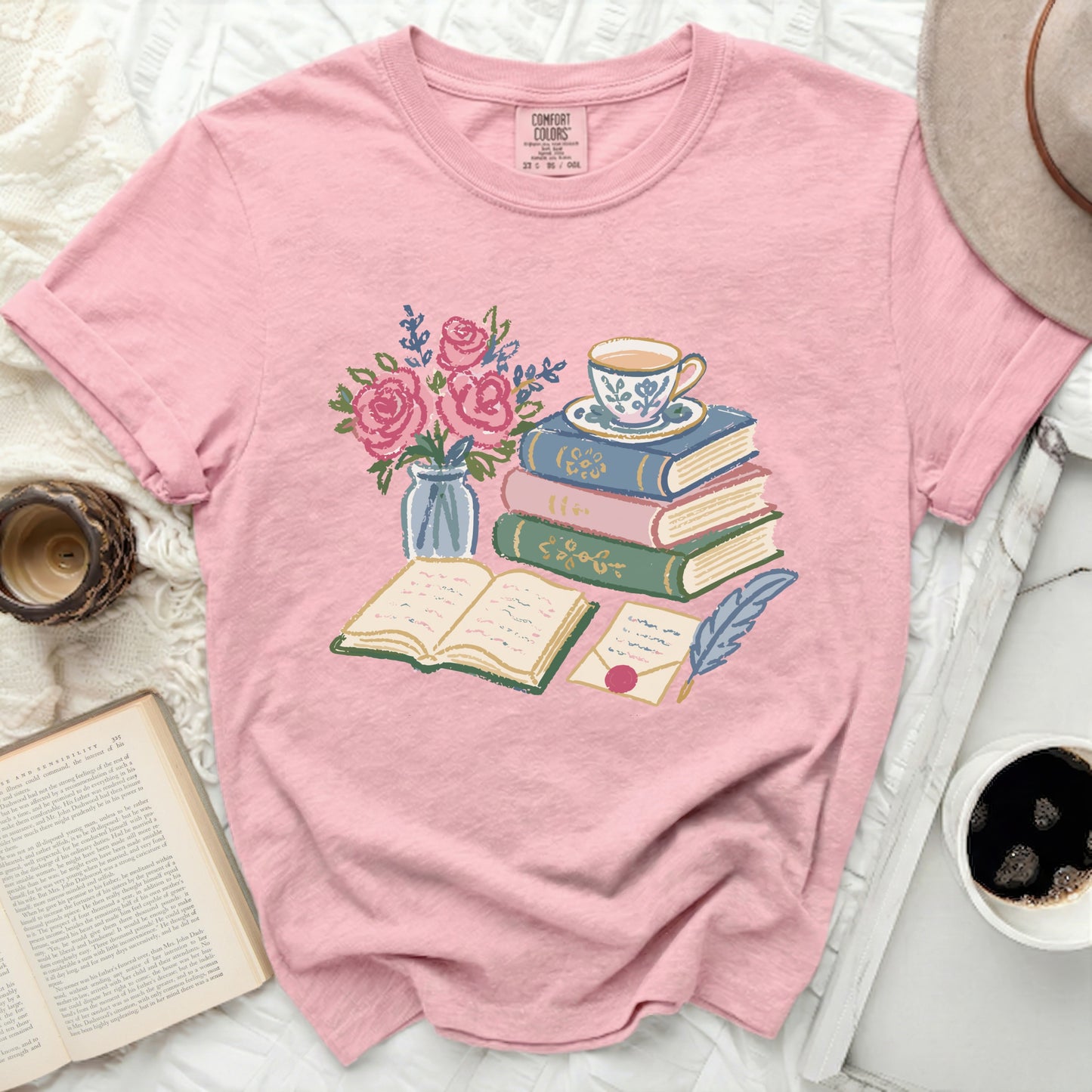 Pink t-shirt with illustration of books, teacup, flowers, and quill.