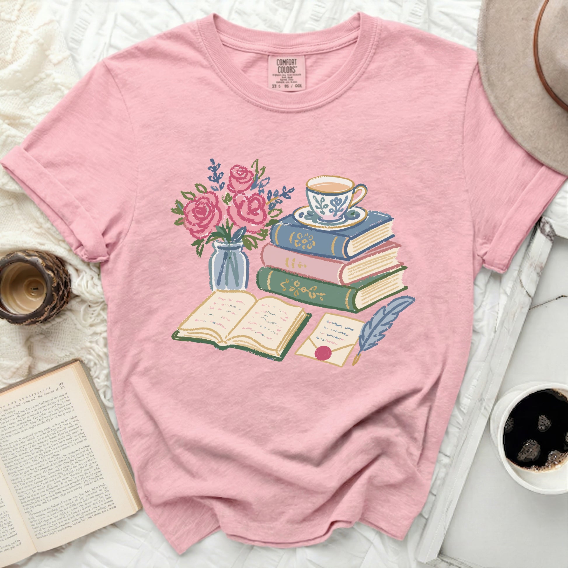Pink t-shirt with illustration of books, teacup, flowers, and quill.