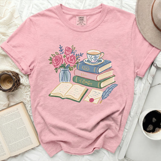 Pink t-shirt with illustration of books, teacup, flowers, and quill.
