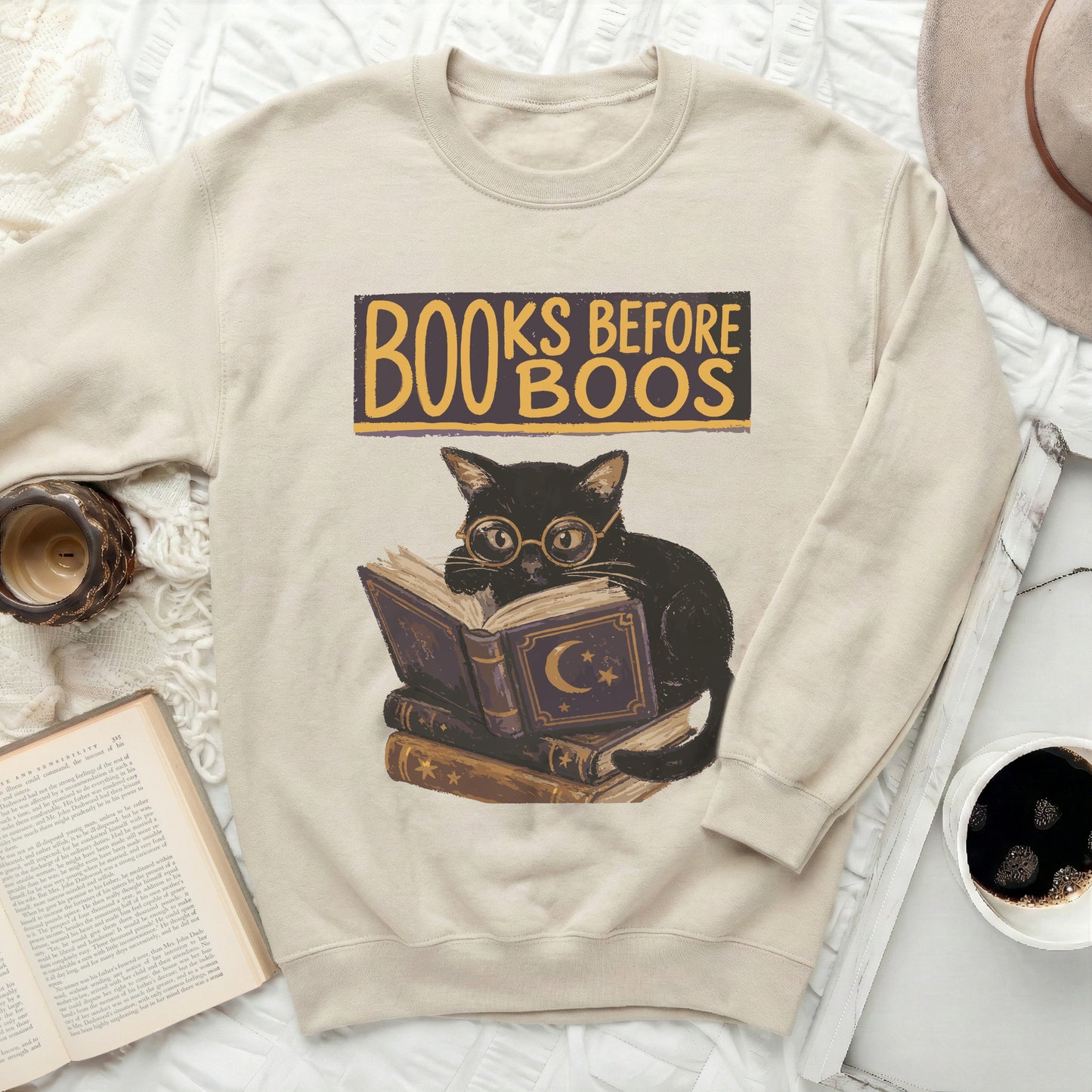 Cream sweatshirt with a black cat reading books, text "Books Before Boos".