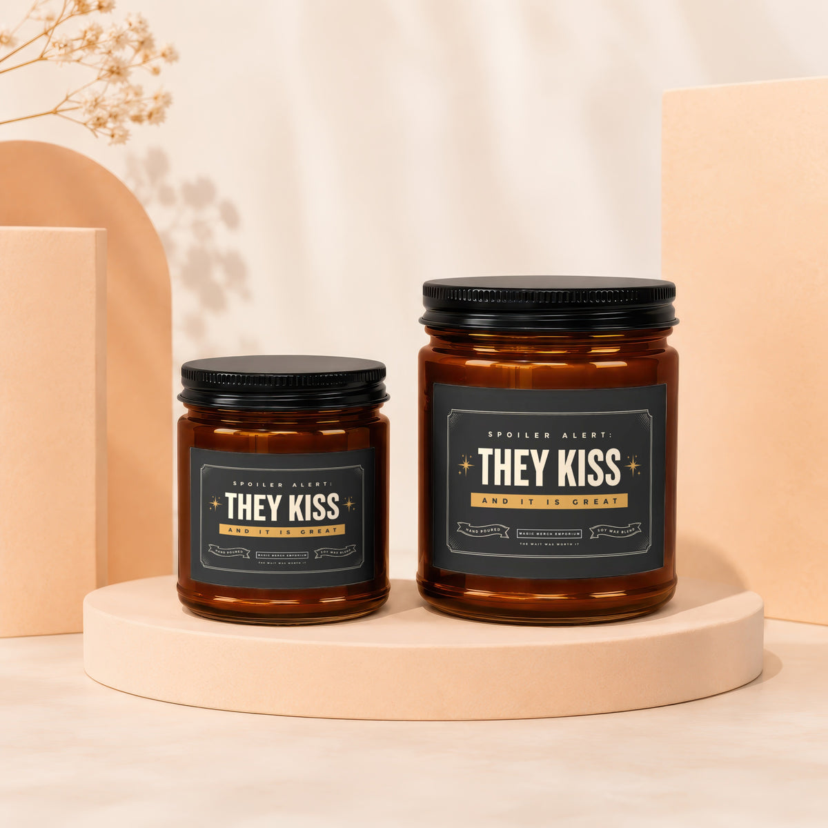 Two amber glass candles with black lids and "They Kiss and It Is Great" labels.