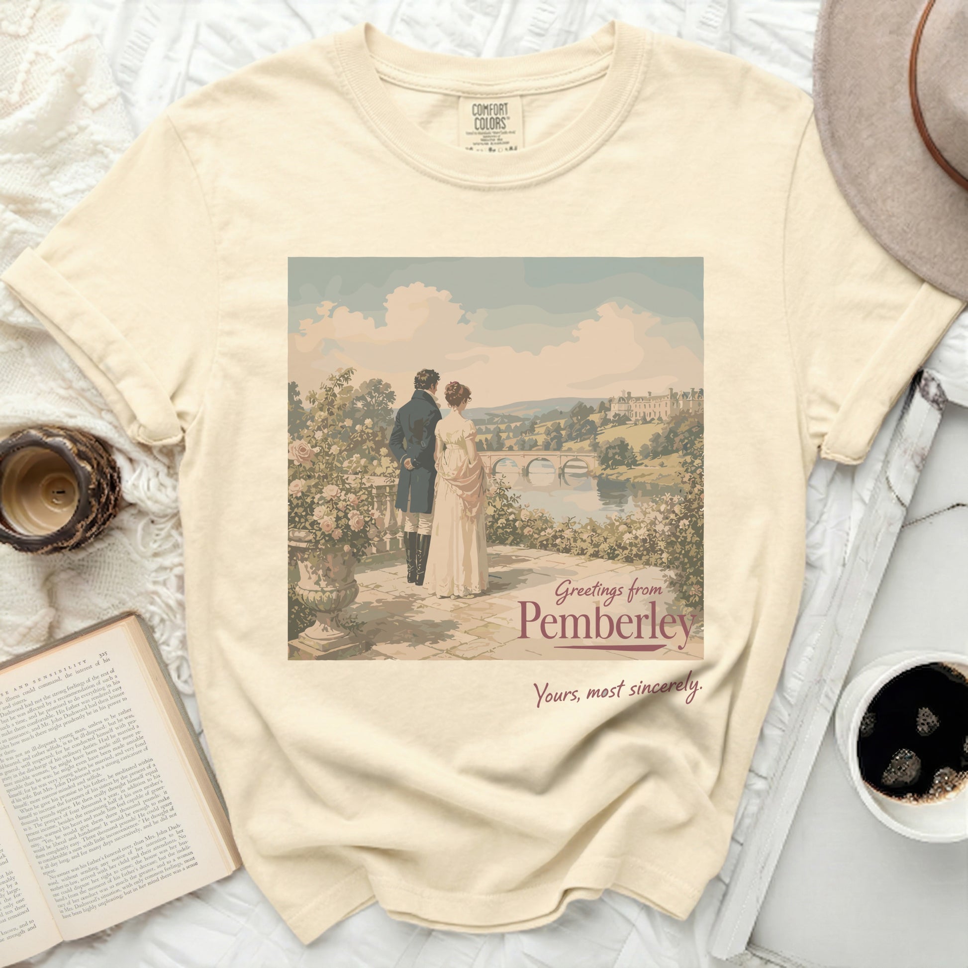 Cream t-shirt with "Greetings from Pemberley" art of a couple overlooking a landscape.