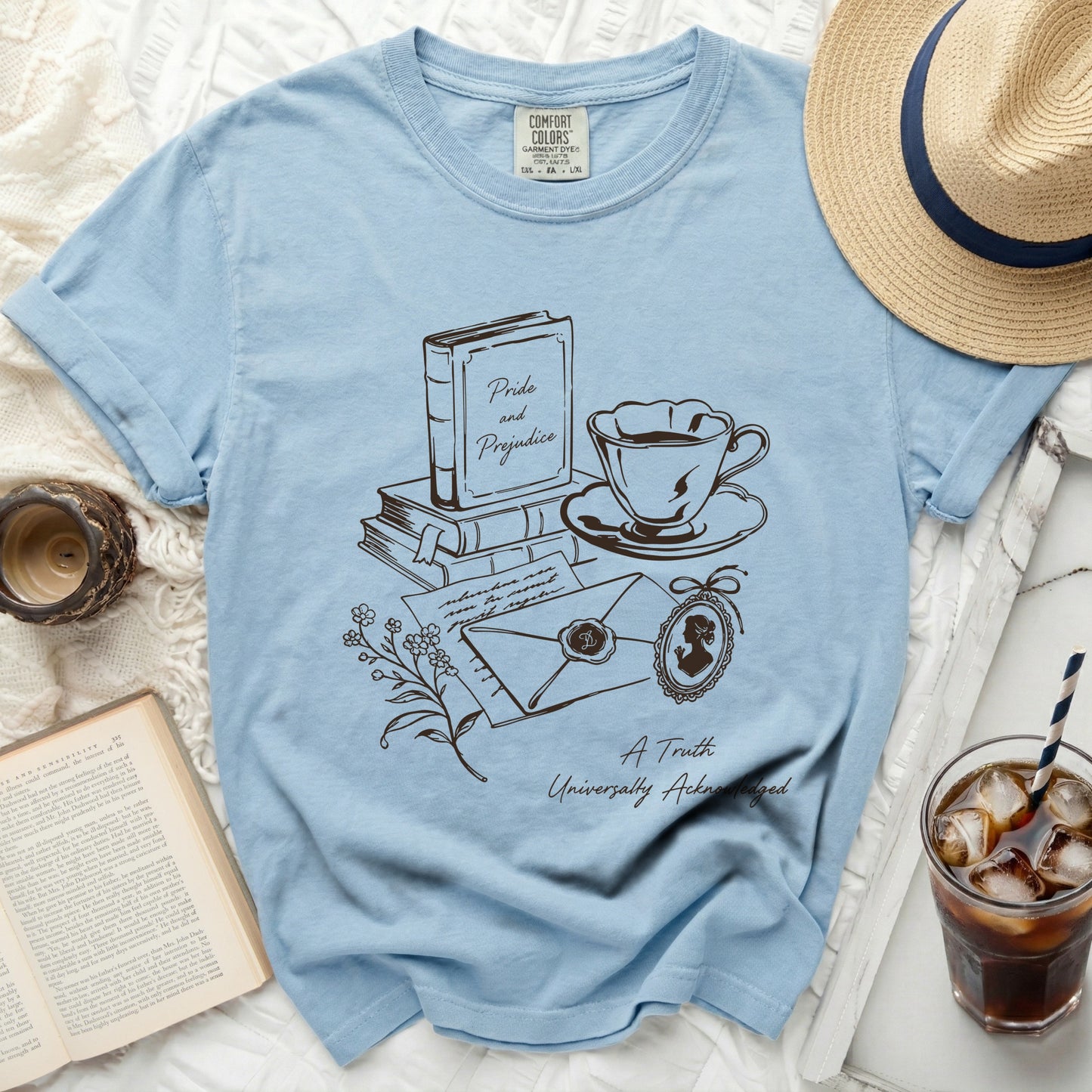 Light blue t-shirt with line art of books, teacup, envelope, and locket.