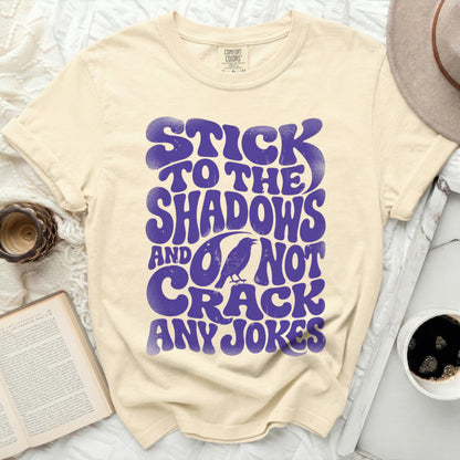 Cream t-shirt with bold purple text: "STICK TO THE SHADOWS AND DO NOT CRACK ANY JOKES."