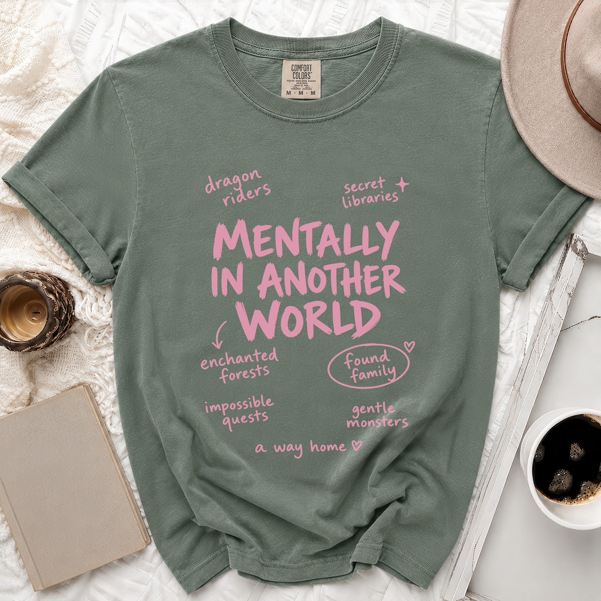 Sage green t-shirt with pink text "Mentally in Another World" and related phrases.