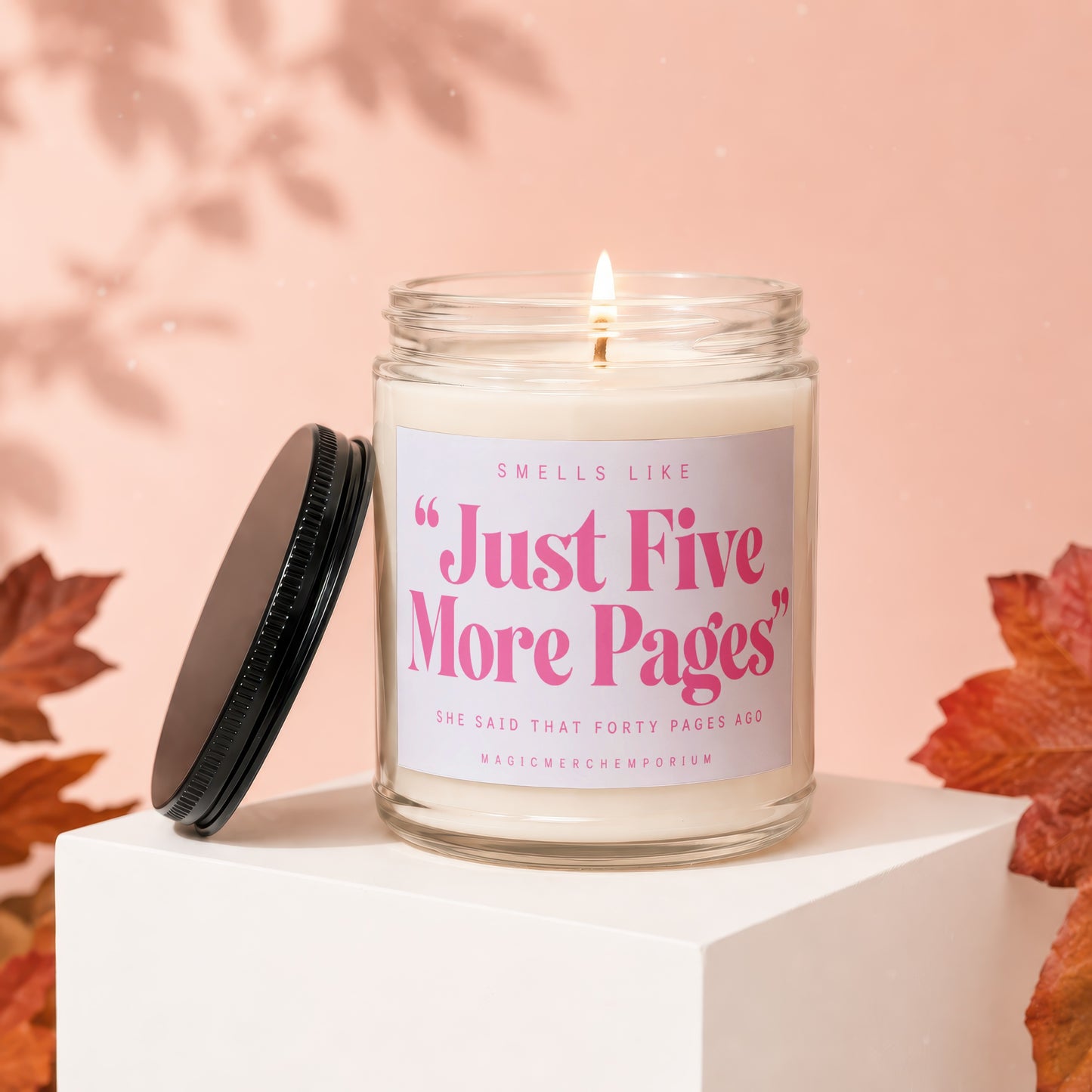 Lit candle in glass jar with "Just Five More Pages" text, black lid beside it.