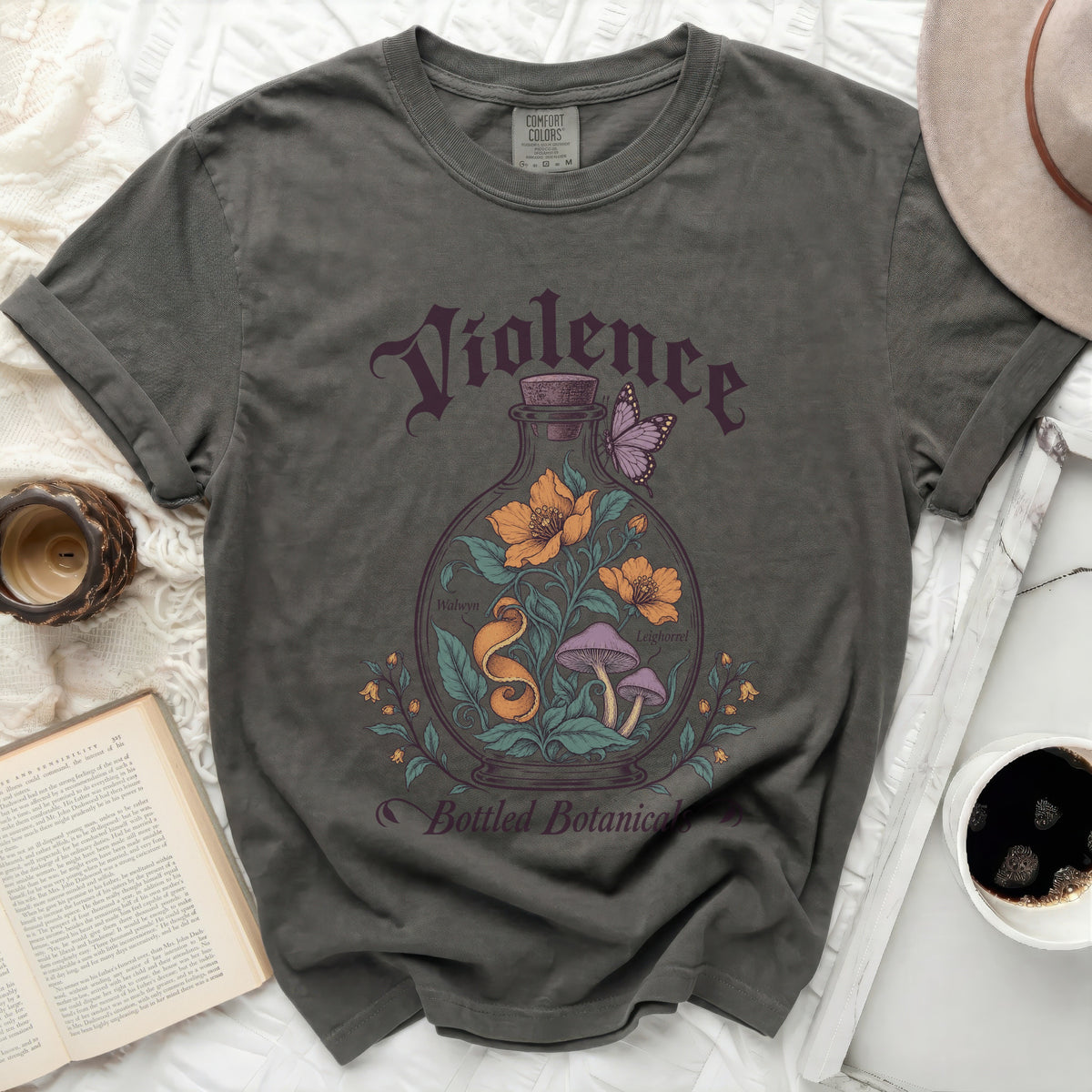 A dark gray crewneck t-shirt featuring a vintage graphic of a glass bottle containing flowers, mushrooms, and a butterfly, with text reading "Violence Bottled Botanicals".