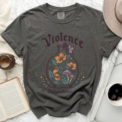 A dark gray crewneck t-shirt featuring a vintage graphic of a glass bottle containing flowers, mushrooms, and a butterfly, with text reading "Violence Bottled Botanicals".