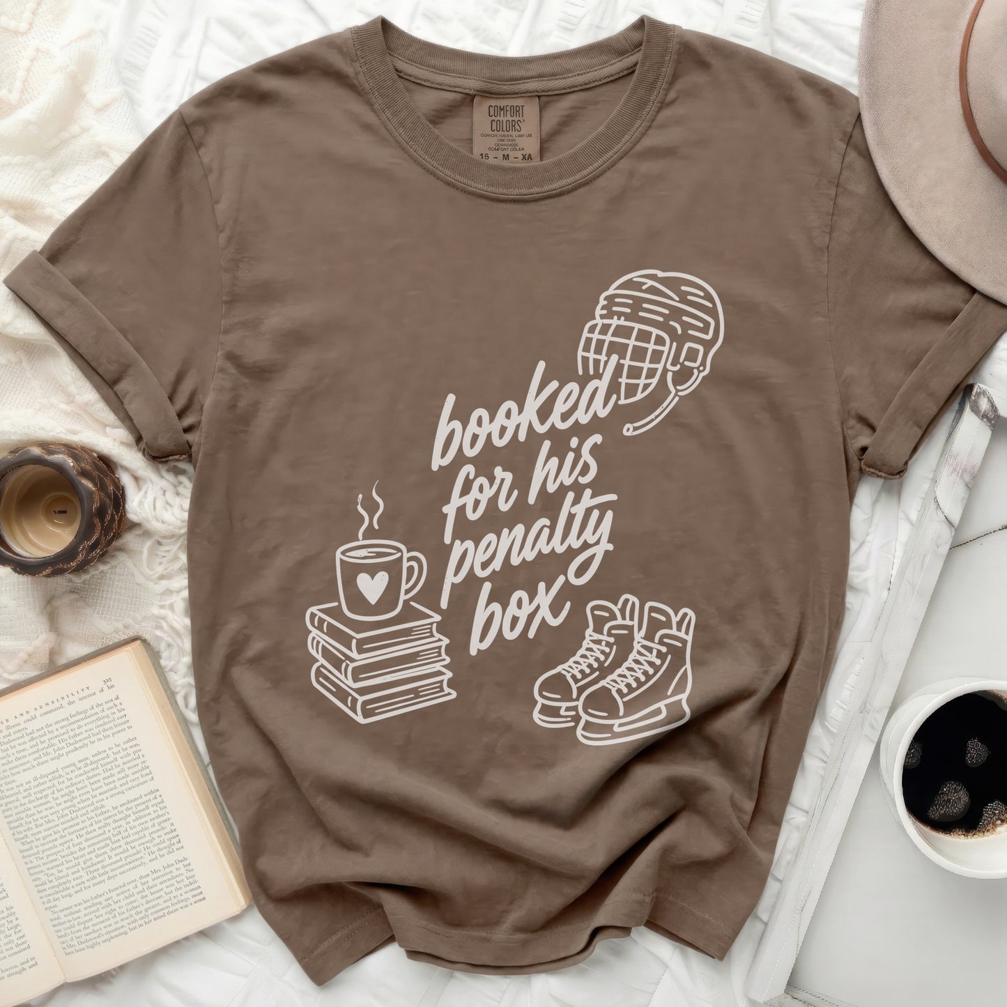 Brown t-shirt with "booked for his penalty box" text, hockey gear, and books.