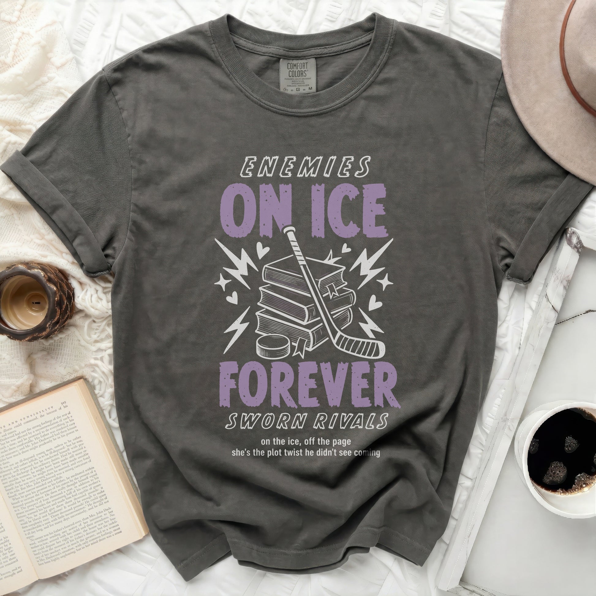 Dark grey t-shirt with "ENEMIES ON ICE SWORN RIVALS" text, hockey stick, and books.