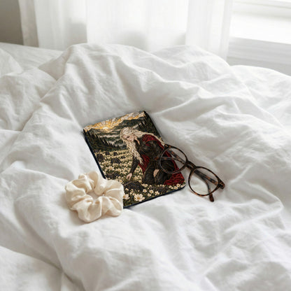 Book with fantasy art of woman in field of flowers and glasses on white sheets.