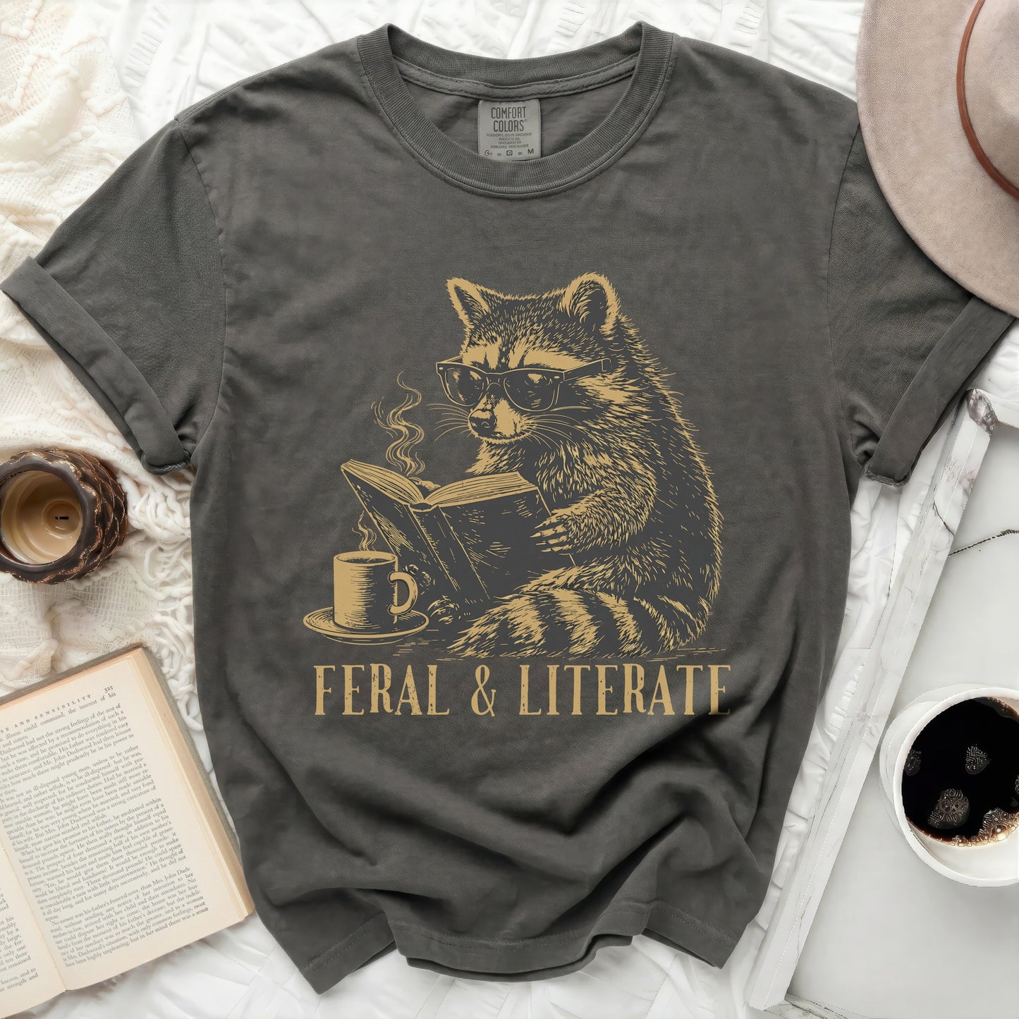 Dark gray t-shirt with a graphic of a raccoon wearing glasses reading a book.