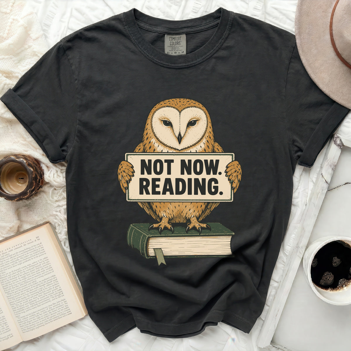 Dark t-shirt with graphic of owl holding sign reading "NOT NOW. READING."