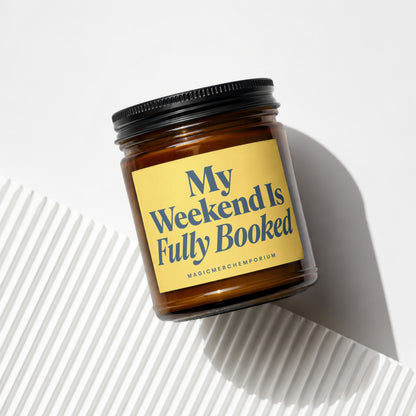 Amber jar candle with black lid and yellow label reading "My Weekend Is Fully Booked".