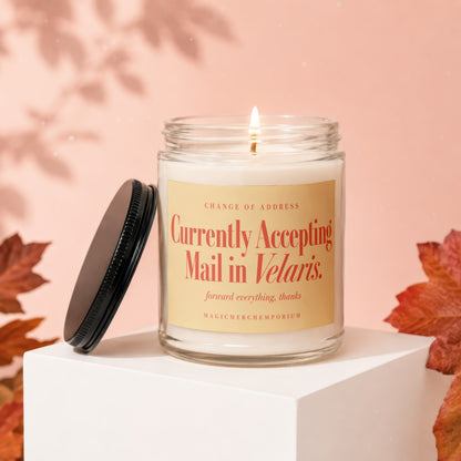 A lit candle in a glass jar with a black lid and yellow label reading Currently Accepting Mail in Velaris.