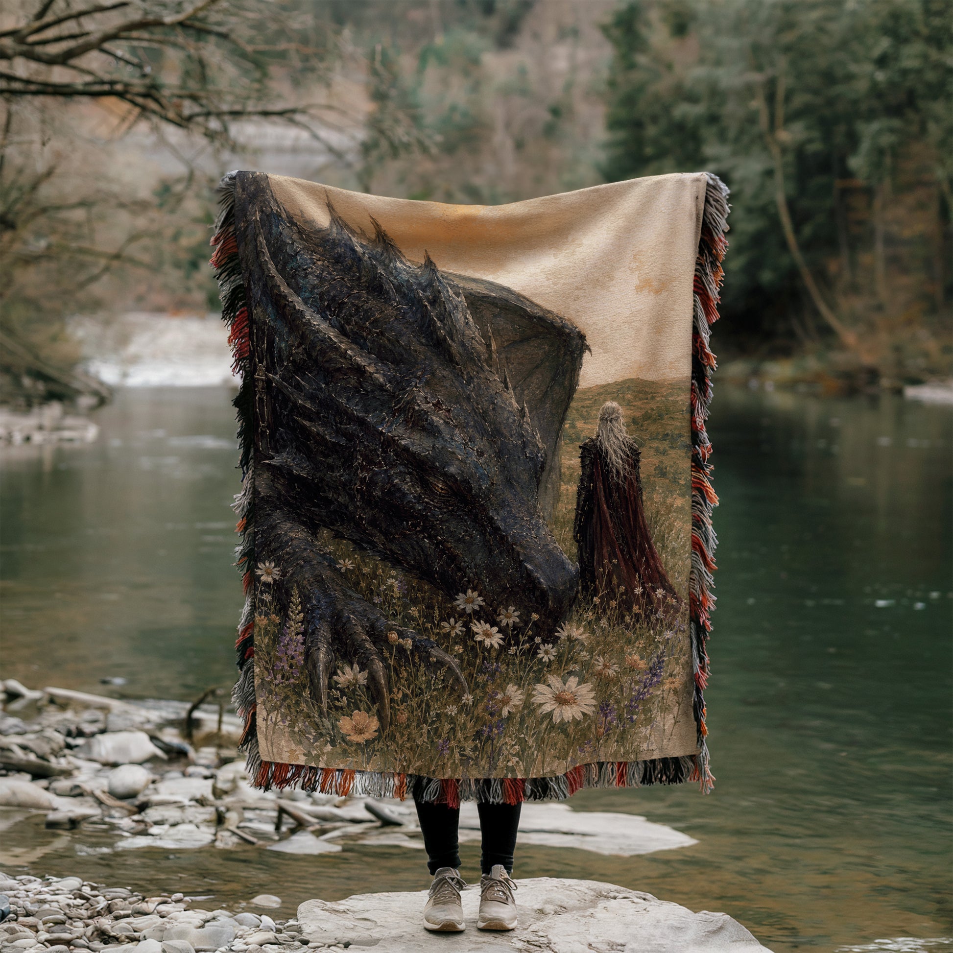A person stands on a rock, holding a large tapestry with a dragon and a woman in a field in front of a river.