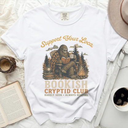 Bigfoot sitting in chair reading book with "Bookish Cryptid Club" text.