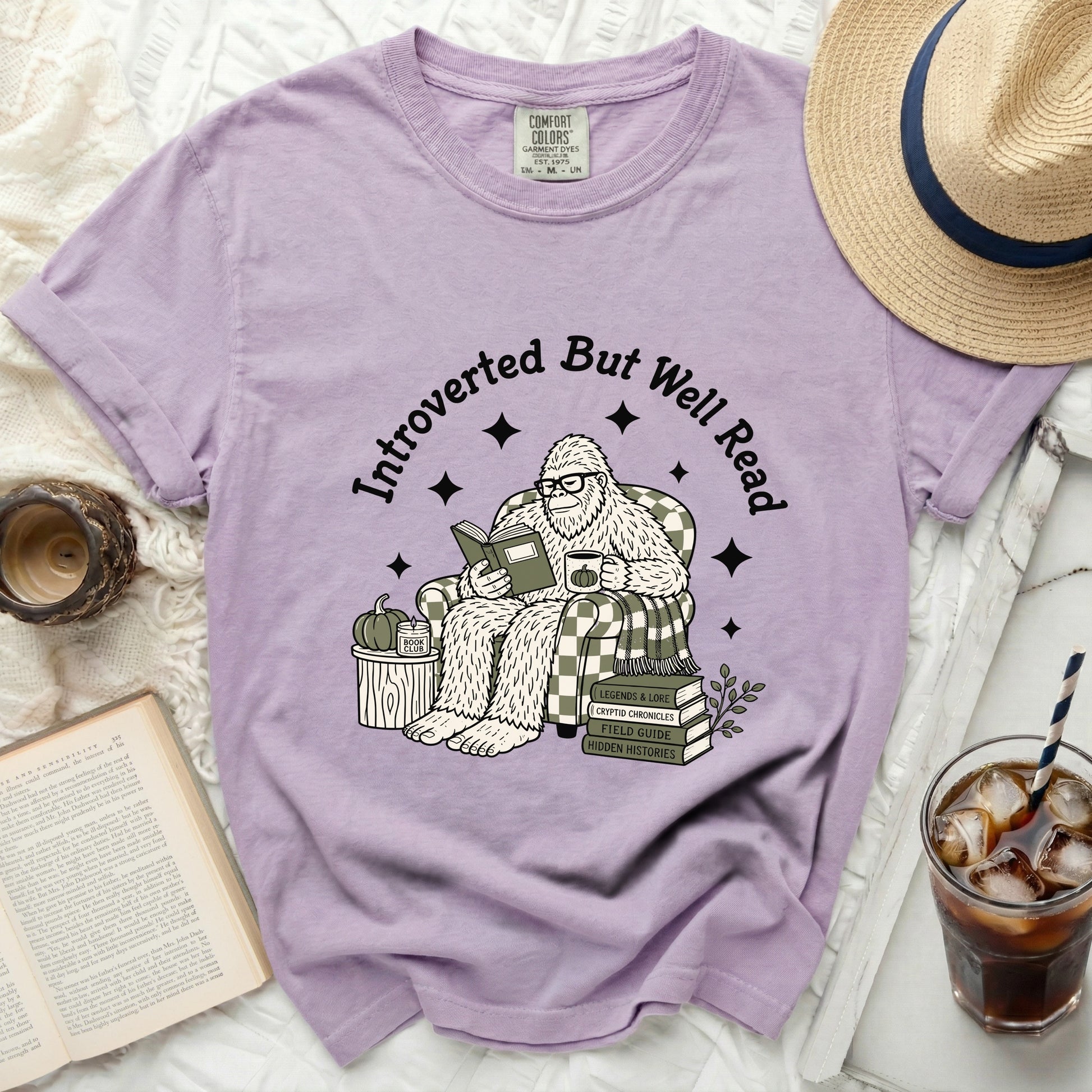 Purple t-shirt featuring a Bigfoot reading a book, sipping coffee, and text "Introverted But Well Read."