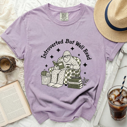 Purple t-shirt featuring a Bigfoot reading a book, sipping coffee, and text "Introverted But Well Read."