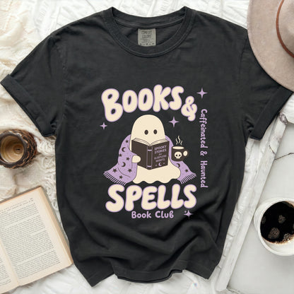 Dark t-shirt with a ghost reading under a blanket for "Books & Spells Book Club".