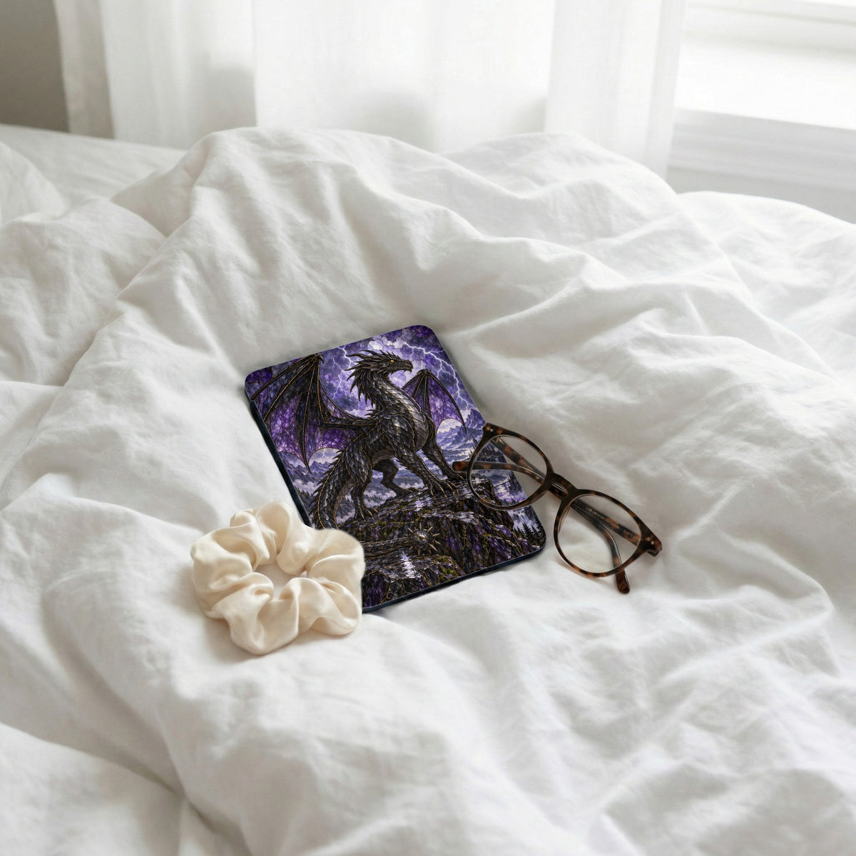 Dragon on rocky perch with stormy sky, glasses, and scrunchie on white bedding.