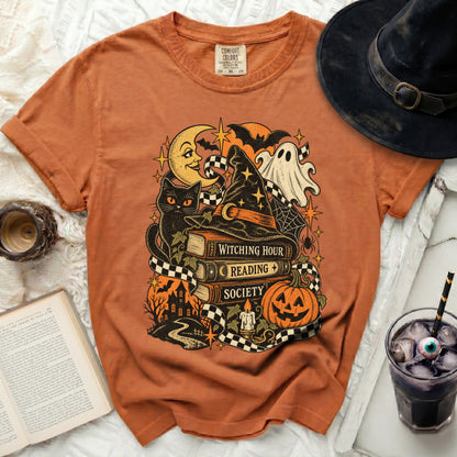 Orange t-shirt with Halloween graphic: witch hat, books, cat, ghost, pumpkin.