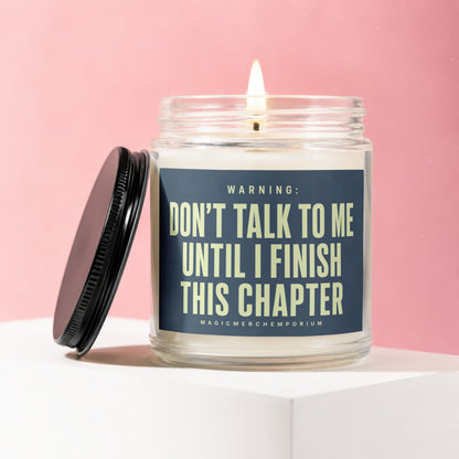 Glass candle with burning wick, lid removed, reads "DON'T TALK TO ME UNTIL I FINISH THIS CHAPTER".