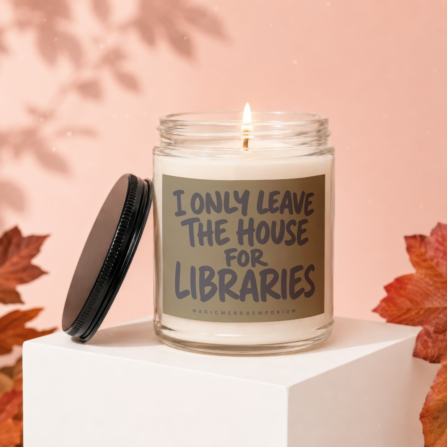 Lit candle in glass jar with lid off, reads "I only leave the house for libraries".