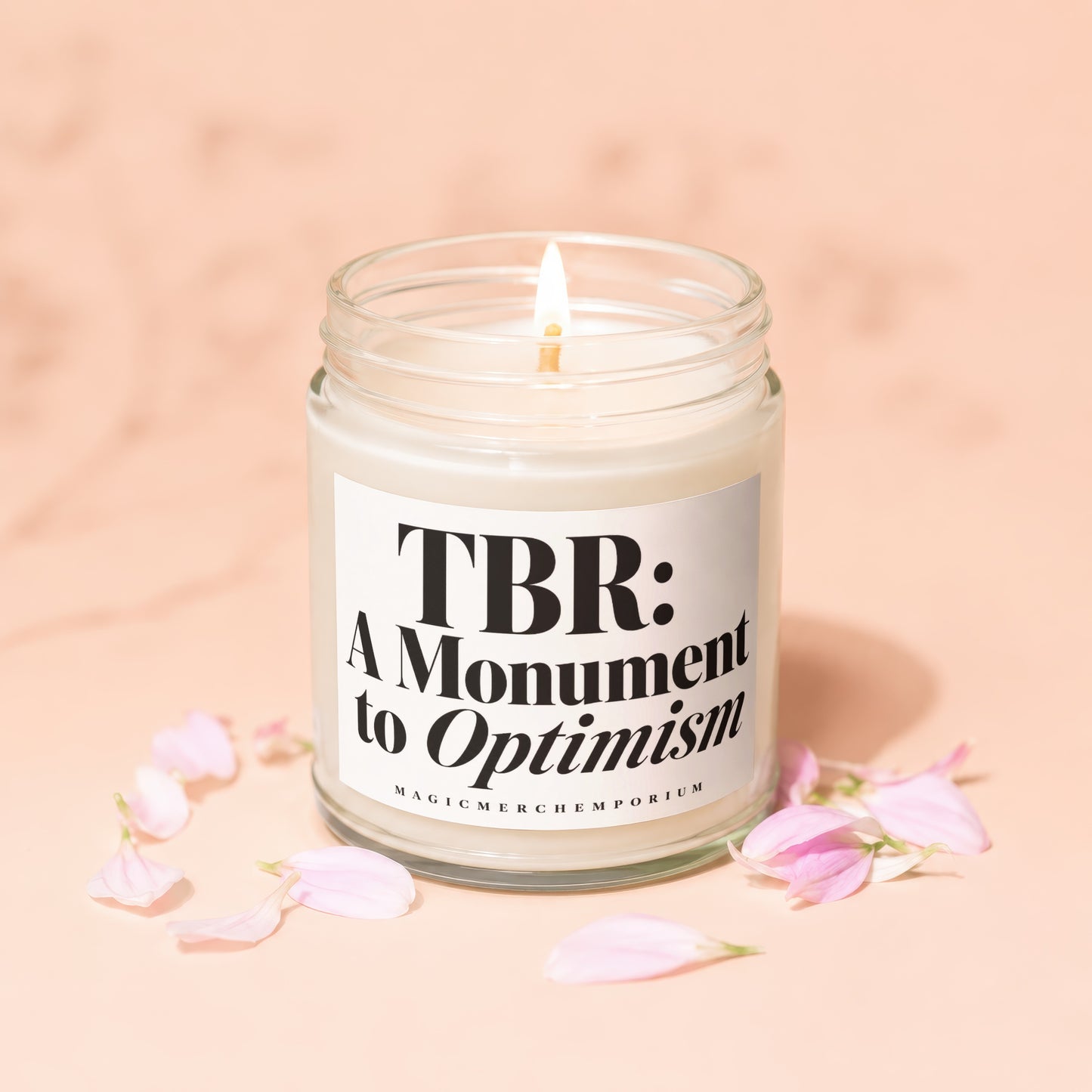 Candle with label "TBR: A Monument to Optimism" surrounded by pink petals.