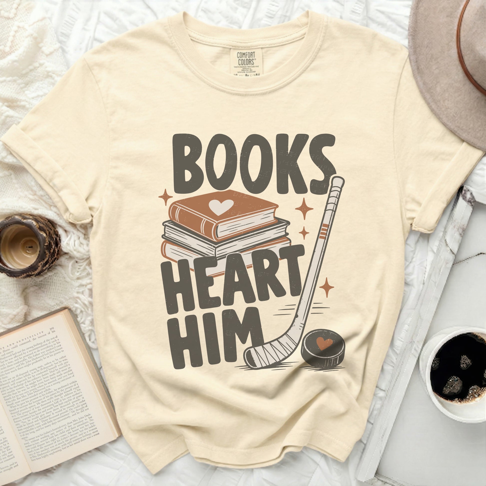 Cream t-shirt with "Books Heart Him" text, books, and hockey stick graphic.