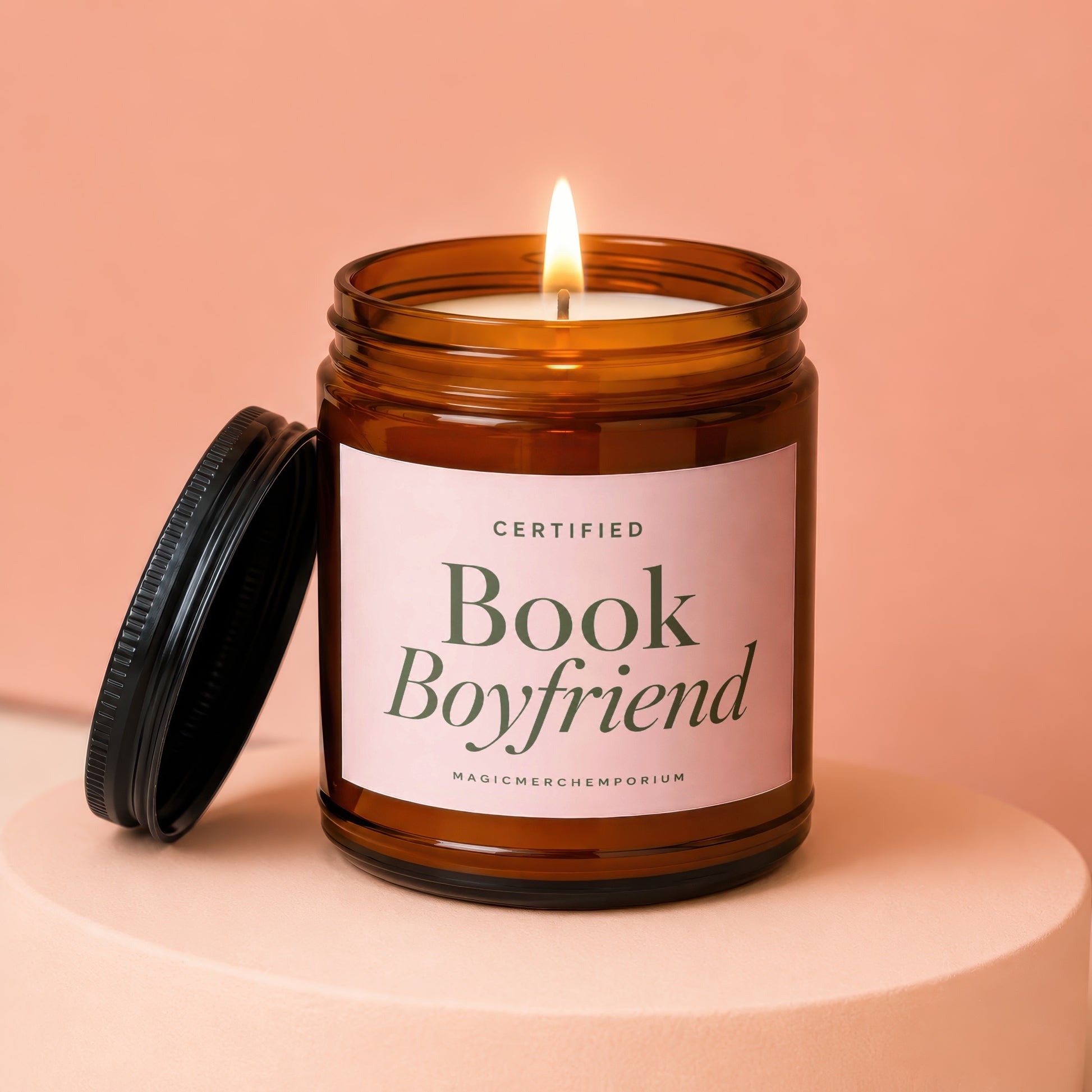 Lit candle in amber jar with pink label reading "Certified Book Boyfriend"