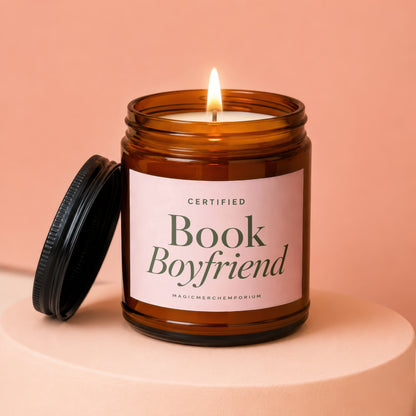 Lit candle in amber jar with pink label reading "Certified Book Boyfriend"