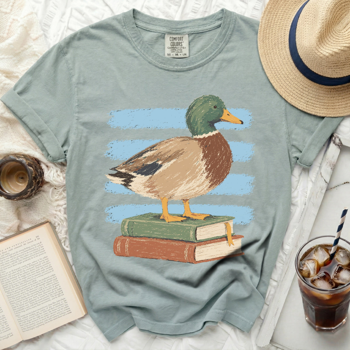 Light blue t-shirt with a graphic of a mallard duck standing on two books.