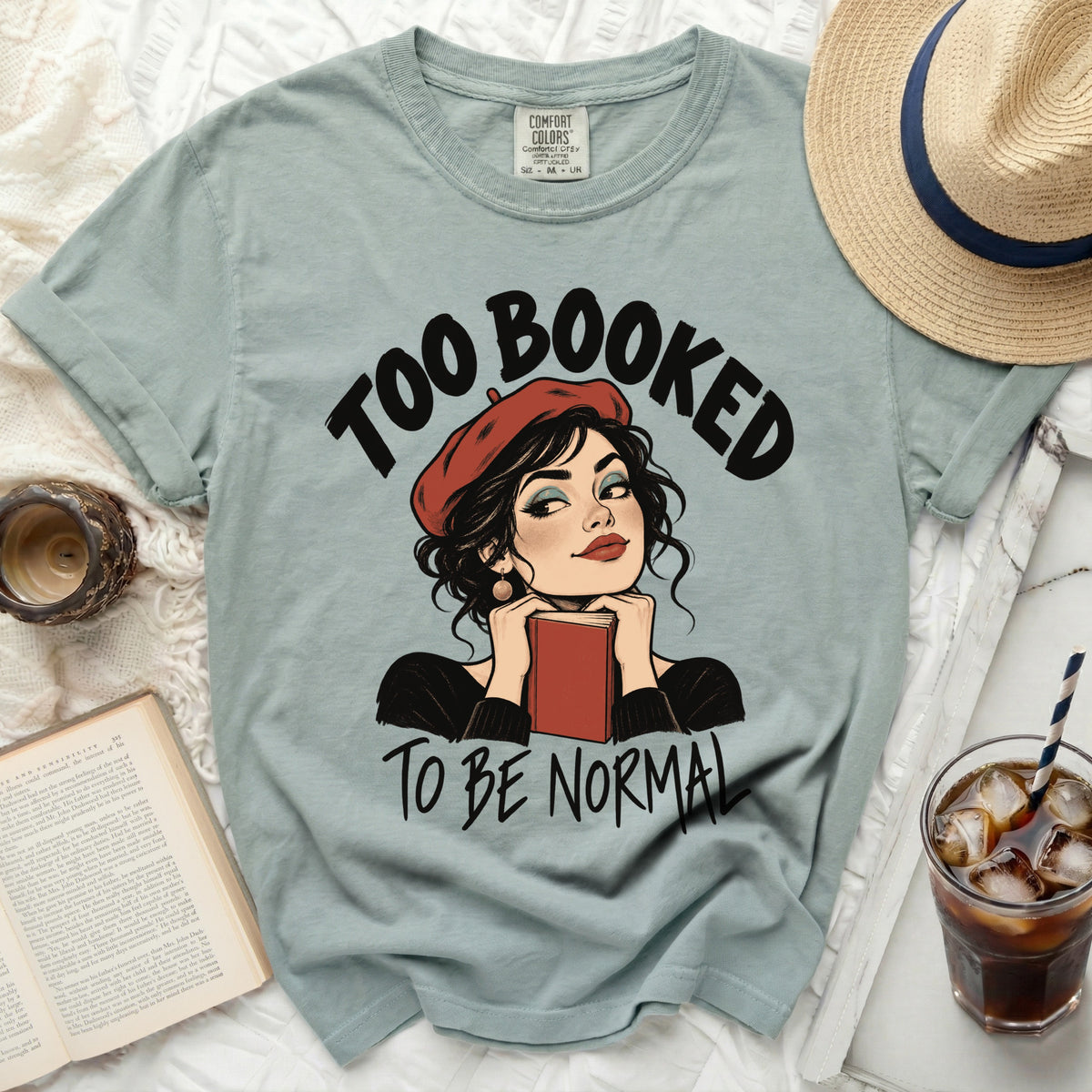 Light blue t-shirt with text "Too Booked To Be Normal" and comic illustration.