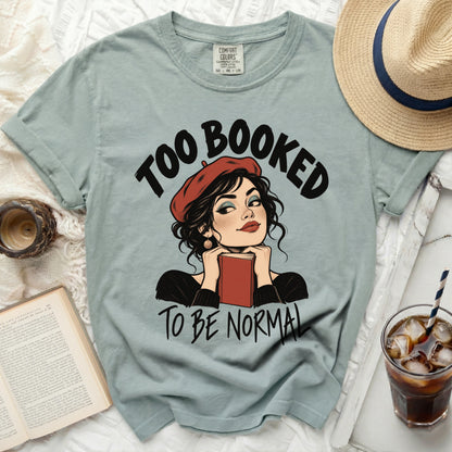 Light blue t-shirt with text "Too Booked To Be Normal" and comic illustration.