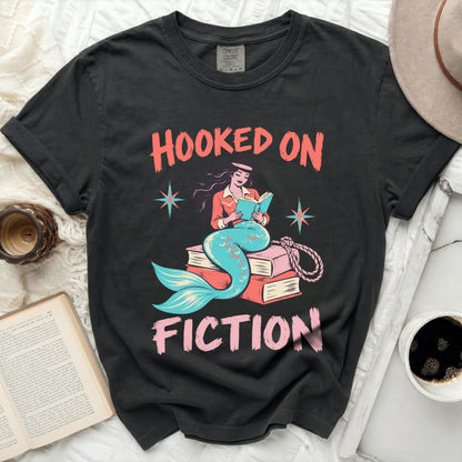 Black t-shirt with "Hooked on Fiction" text featuring a mermaid reading on books.