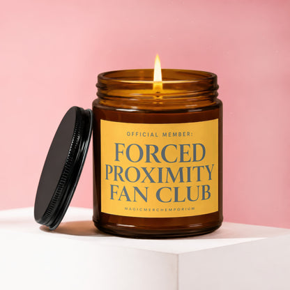 Amber jar candle with lit wick, lid off, reading "OFFICIAL MEMBER: FORCED PROXIMITY FAN CLUB".