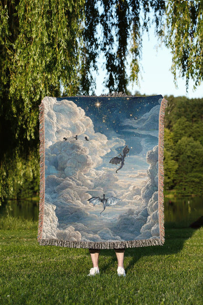 A person is standing in a grassy area, holding a large tapestry or blanket that features a painting of a night sky with clouds and two flying dragons.